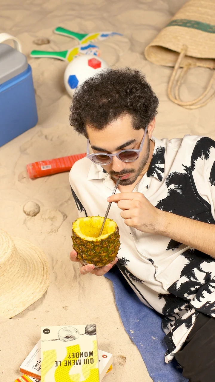 Climate and Pollution: Baha Lajmi drinking from a pineapple on a sandy beach